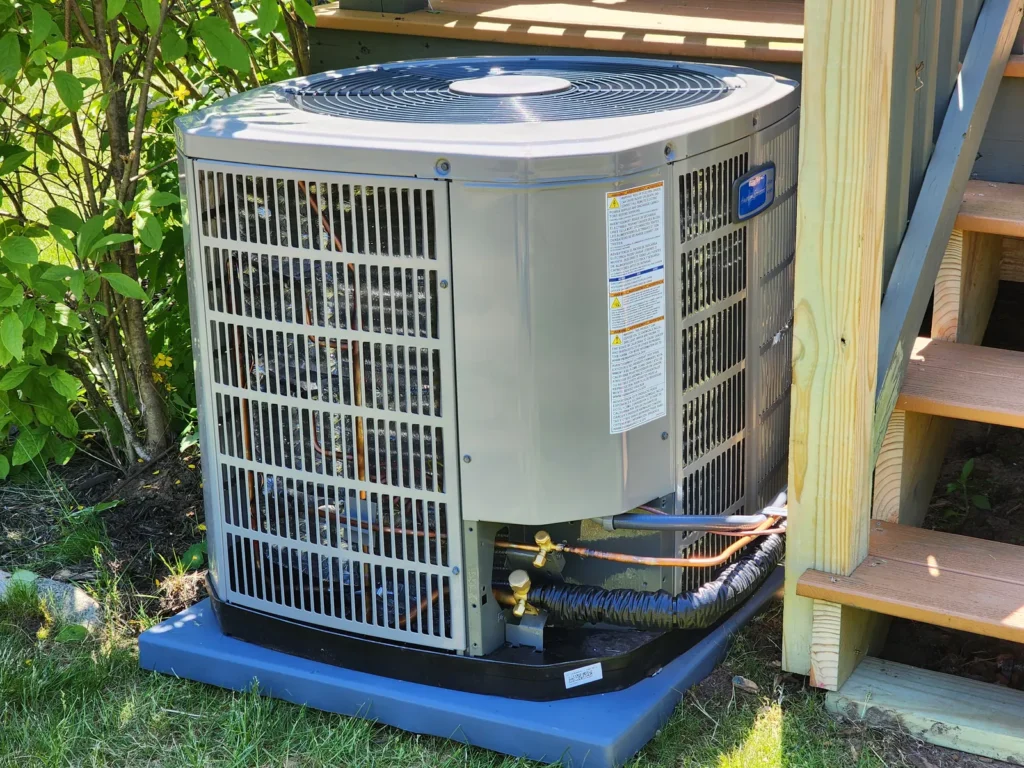Central air conditioner condenser on a pad by a deck