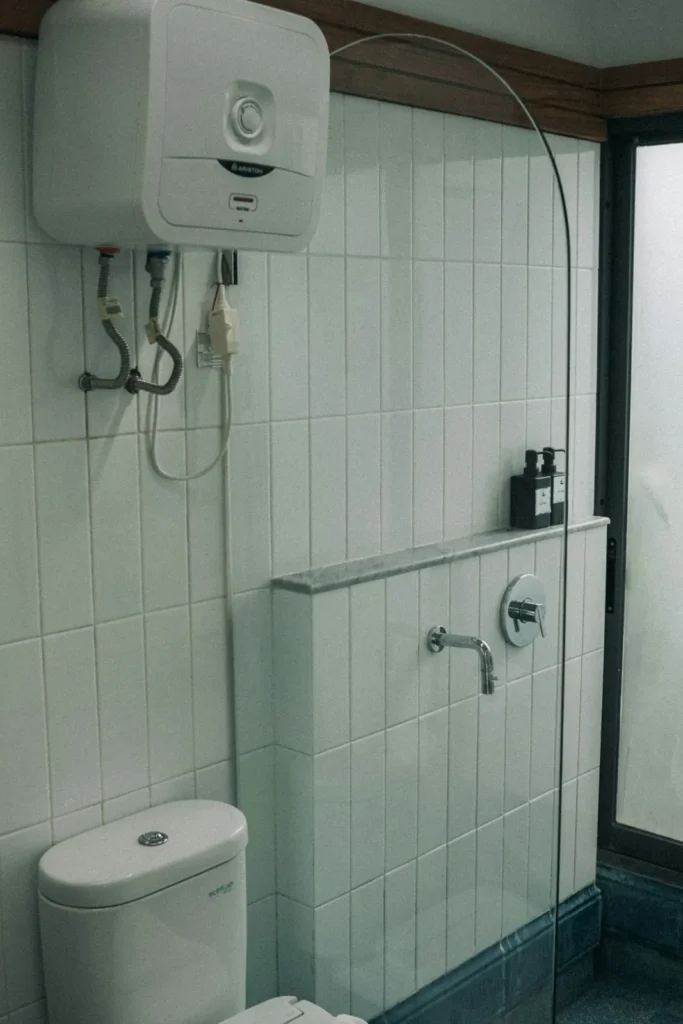 Electric water heater mounted on a white tiled wall in a shower room