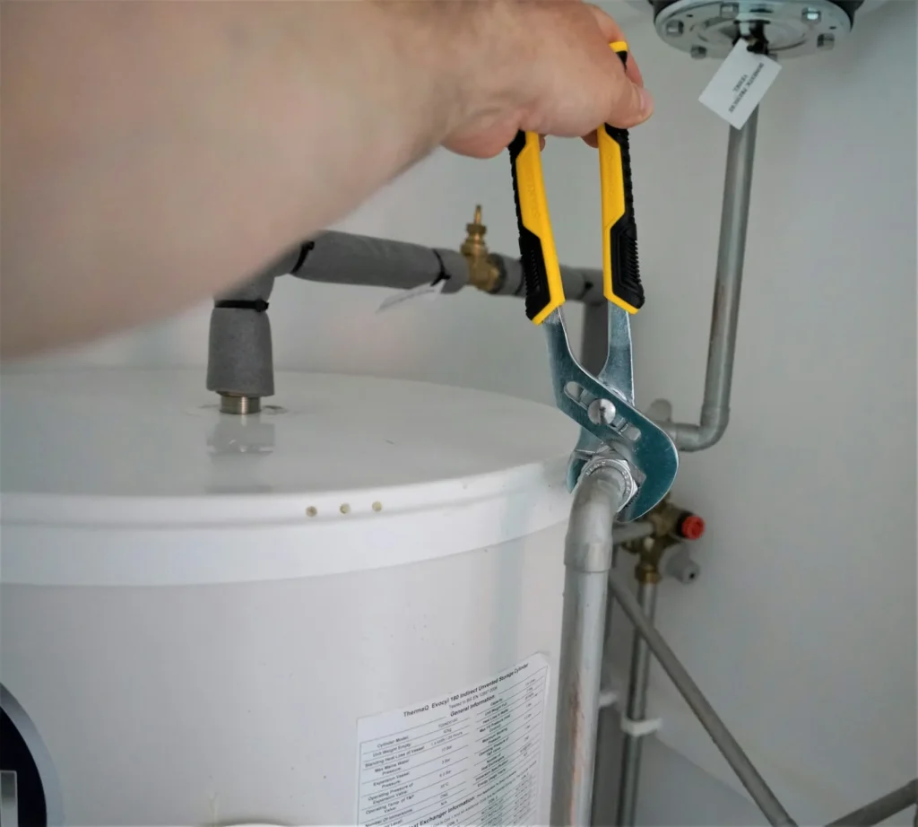 Technician tightening a water heater supply fitting with a wrench during repair